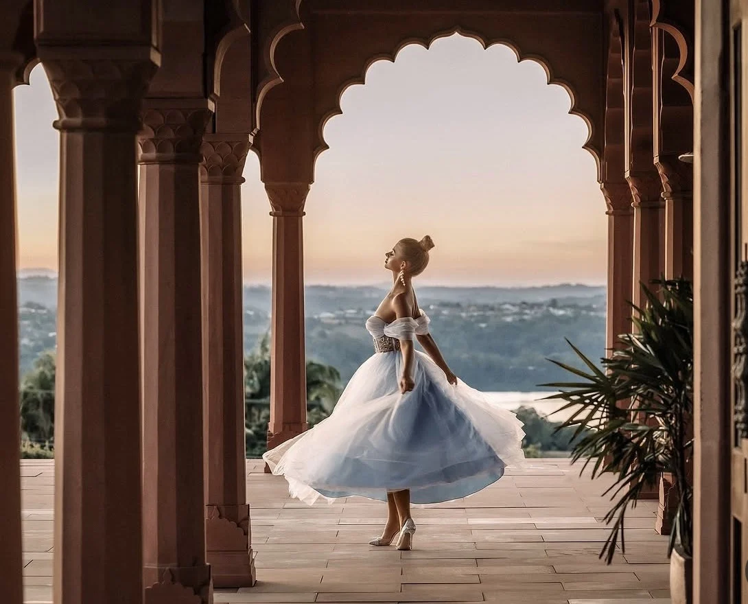 A model twirling in a pale blue gown beneath the palace's scalloped archways at sunset