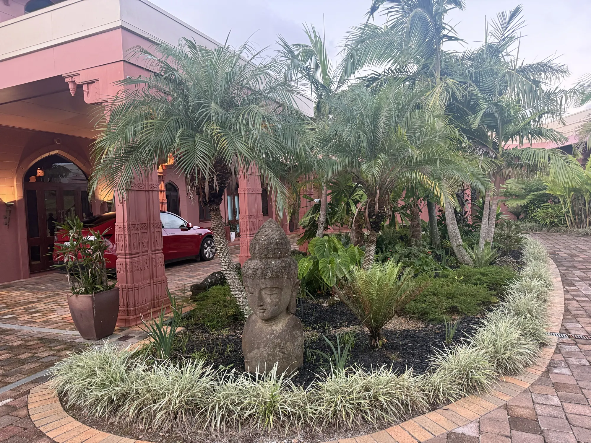 The gardens at Jodha Bai, a stone Buddha bust framed by palms at the entrance driveway