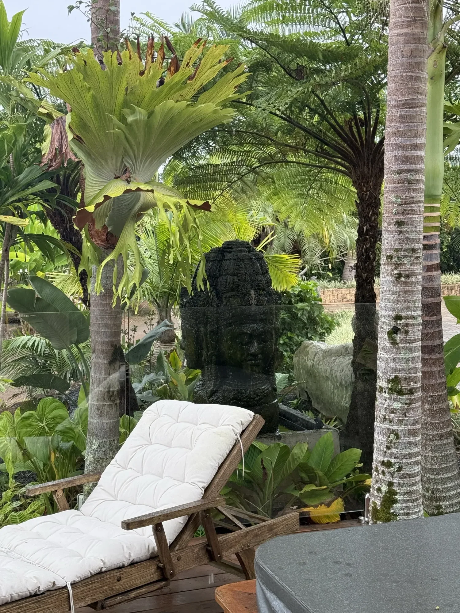The gardens at Jodha Bai, a carved stone statue beside the timber deck lounge chairs