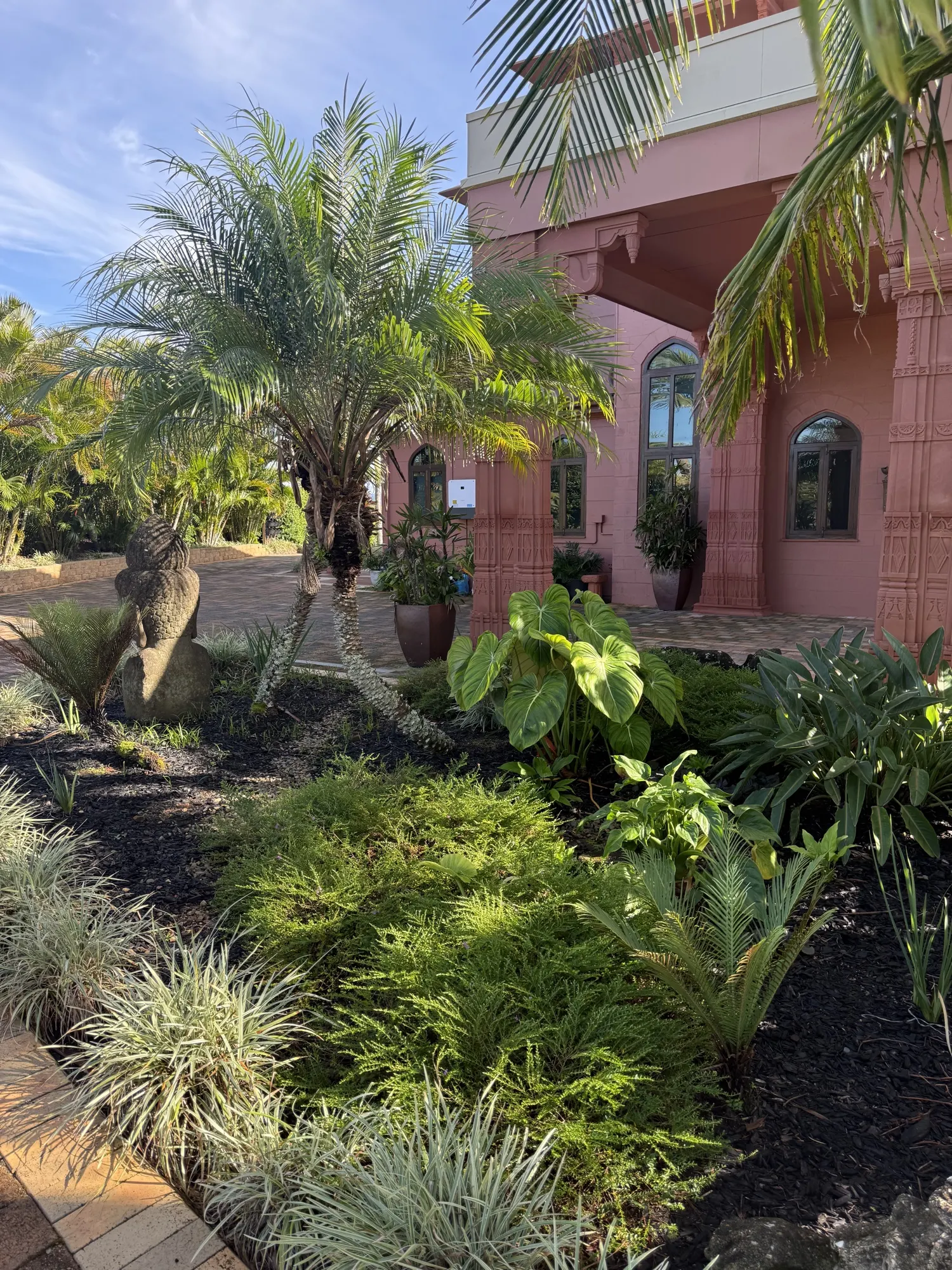 The gardens at Jodha Bai, palm trees and a stone statue beside the sandstone facade