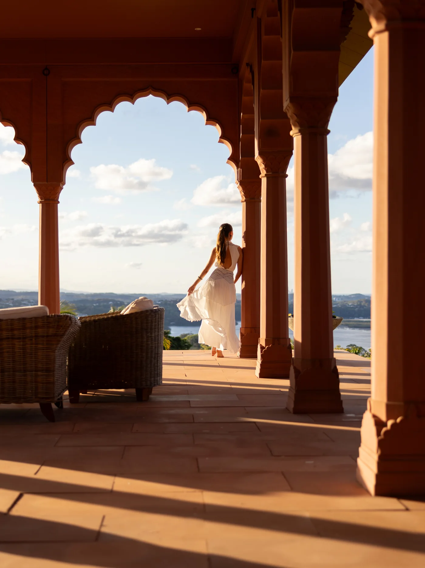 A model in a flowing white dress beneath the palace's scalloped archways at sunset